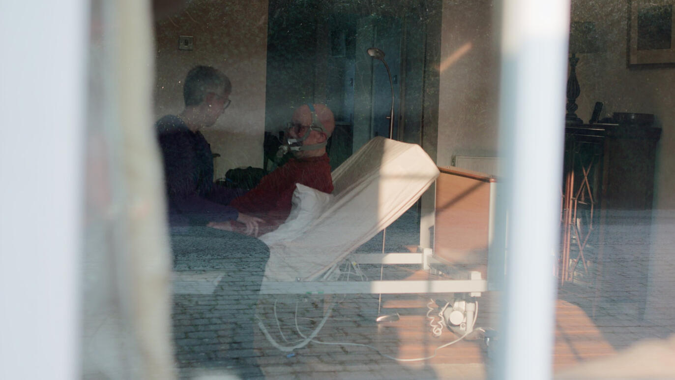 A wife comforts her terminally ill husband in a bed